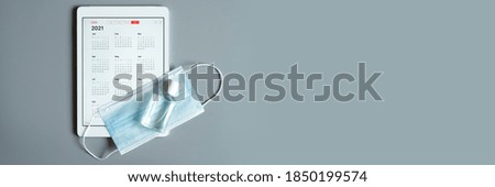 a tablet with an open calendar for 2021 year and protective medical mask and hand sanitizer on a gray background. covid-19 coronavirus protection concept in 2021. banner. space for text