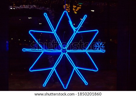 Neon illuminated bright metallic snowflake closeup on dark background, decoration on night city, festive symbol