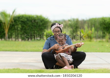 A black American daughter sitting on her mother's lap Playing an acoustic guitar in the park