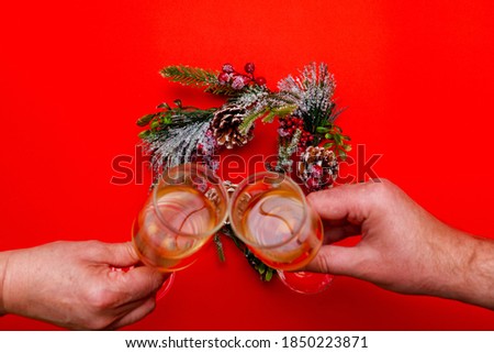 Top view Two male and female hands holds glasses of champagne, flat lay wreath on a red background