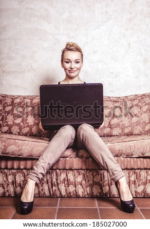 Technology internet modern lifestyle concept. Full length young business woman or student girl using laptop working on computer sitting on retro couch. Indoor. Vintage photo.
