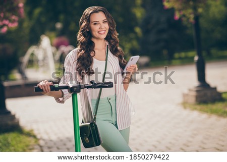Photo of charming cheerful sporty girl drive segway hold telephone wear striped shirt green jeans bag enjoy summer fresh air outside