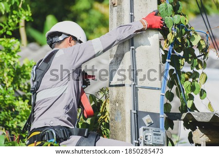 Electrical utility worker fixing or repairing a problem on power line against, wearing equipment PPE, full safety harness full body,