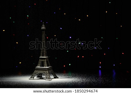Miniature of the Eiffel Tower. In the dark - a ray of light from above and against the background of shining garlands. Eiffel Tower in the New Year. Macro photography. 