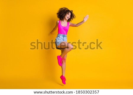 Full body photo of attractive curly lady jump up high dancing students party delighted emotions wear pink tank top denim mini skirt shoes isolated vivid bright yellow color background