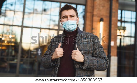 Outdoor portrait of an attractive young man in winter clothes and protective medical face mask. Prevention of Covid-19 coronavirus infection. A handsome guy on the street during a new flu epidemic.