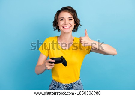 Photo of funny girl hold joystick raise thumb up toothy smile wear yellow t-shirt isolated blue color background
