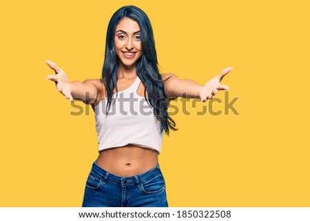 Beautiful hispanic woman wearing casual clothes smiling cheerful offering hands giving assistance and acceptance. 