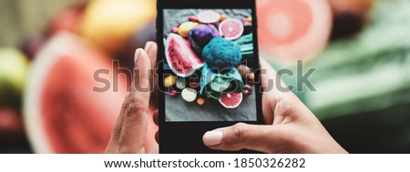 Table with delicious meals and plates. Fruits and vegetables. Woman's hands with phone taking food photo