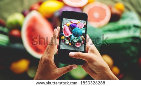 Table with delicious meals and plates. Fruits and vegetables. Woman's hands with mobile phone taking food picture