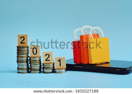 close up stack of coin, wooden 2021 text block, shopping bag and smartphone on blue background, saving and manage money for new year season, e-commerce and online technology  concept
