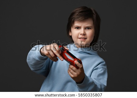 Portrait of Cute boy 10-12 years old, dressed in casual clothes, standing with joystick in hands playing and looking at camera. Childhood, facial expression concept. Studio shot, gray background