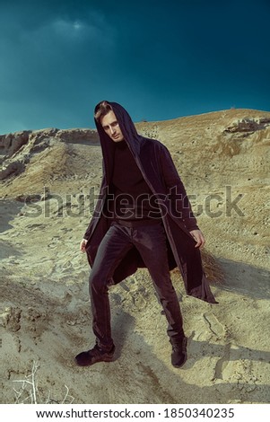 Men's fashion. Handsome brunet man stands in a desert in black clothes.