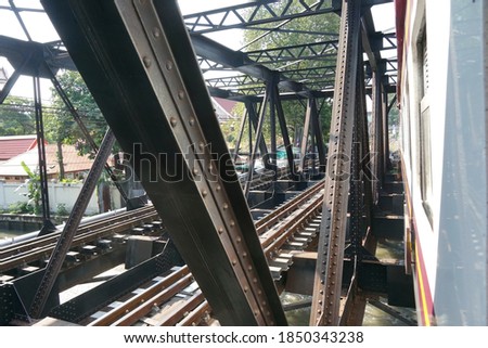 Selective focused, steel bridge of railway tracks for train crossing canal in Bangkok. Canal, building tree background. Concept of steel bridge, railway tracks, train tracks, vintage bridge.