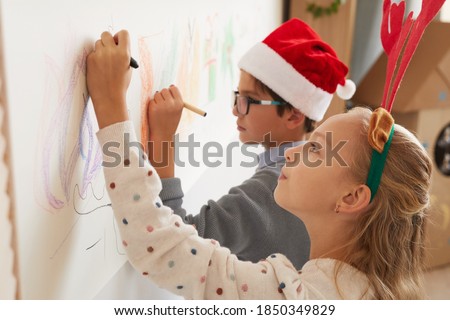 Side view portrait of boy and girl drawing on walls while wearing Santa hats and antlers for Christmas, copy space