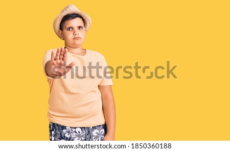 Little boy kid wearing summer hat and hawaiian swimsuit doing stop sing with palm of the hand. warning expression with negative and serious gesture on the face. 
