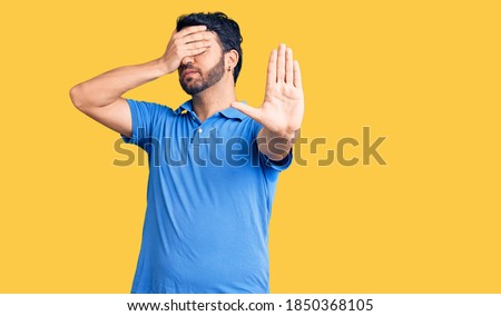Young hispanic man wearing casual clothes covering eyes with hands and doing stop gesture with sad and fear expression. embarrassed and negative concept. 