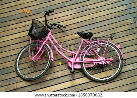 The pink bike lies on the wooden deck.