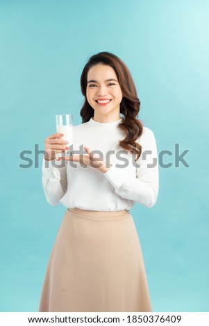 Portrait of a happy Asian woman drinking a glass of milk. Standing in front of a blue wall.