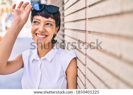 Young woman with short hair smiling happy outdoors wearing sunglasses
