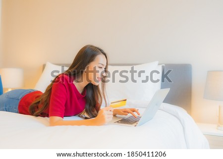 Portrait beautiful young asian woman use computer laptop with credit card on bed in bedroom interior