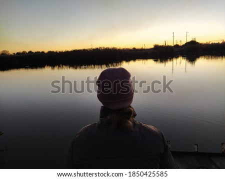 Silhouette of a young woman on the background of the river at sunset. Back view