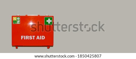 Banner with orange first aid case labeled in English language First Aid hanging on the wall for safety measures with copy space for text