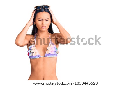 Young beautiful latin girl wearing bikini and sunglasses suffering from headache desperate and stressed because pain and migraine. hands on head. 