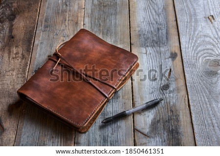 The leather book on the wood table. Handmade paper diary in a brown leather cover on an old vintage wooden table surface background.