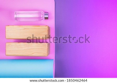 Top view of blue pink yoga mat, two wooden blocks and eco reusable glass water bottle on neon colored pink purple background. Yoga, pilates or sport concept. Flat Lay. Space for text.