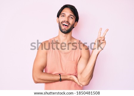 Handsome hispanic man wearing casual clothes smiling with happy face winking at the camera doing victory sign. number two. 