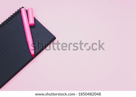 A high angle shot of a notebook and a pink marker on a pink surface