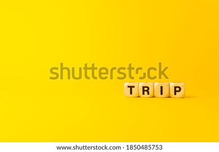 The word trip written with natural wooden dices on the right side of a yellow background