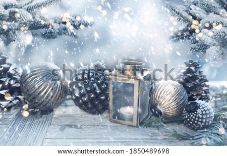 Christmas decoration on wooden table with fir branches in a snowy garden. Cold blue winter background with snow flakes and golden bokeh for christmas and advent concepts with space for text.