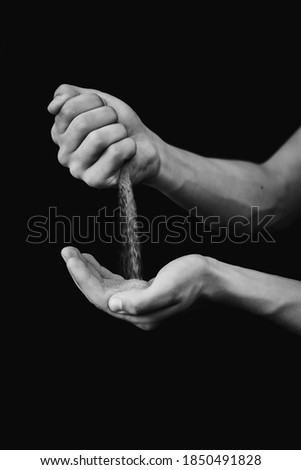 black and white photograph of hands with sand on a black background