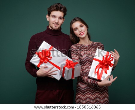 Beautiful young woman, evening makeup stylish dress , brunette, and young man in sweater, gift boxes red silk bows New Year, Christmas. Fashion photo. Green background. New year's Christmas cap