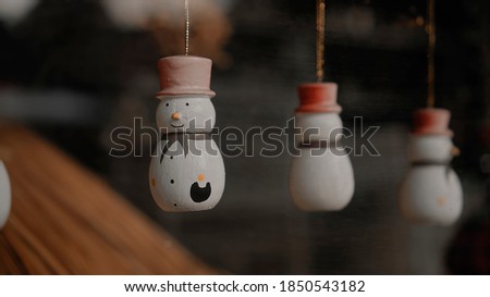 Little white Christmas toys snowmen hang on a thread behind the glass in the house