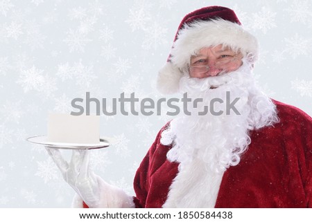 Santa Claus holding a silver platter with a blank note card, over a snow flake background with snow effect.