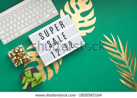 12.12 Super Sale text on white Lightbox, keyboard, computer mouse, gift box, gold tropical leaves Monstera, green paper background. Singles day concept. Online shopping of China. Top view, copy space.