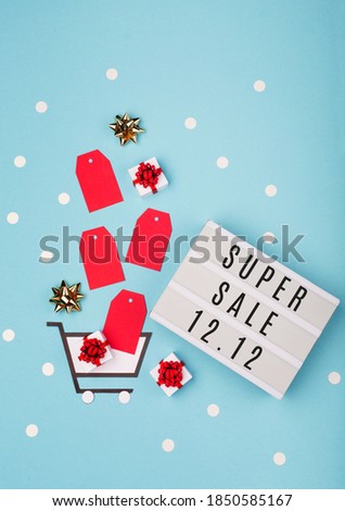 12.12 Super Sale text on white lightbox, shopping trolley, gift boxes and red tags on blue paper background. Double 12 Mega sales day concept. Top view, flat lay, copy space.