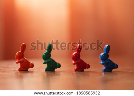 Horizontal photo of multicolored hare wax pencil figurines, symbolizing the queue, on orange background on wooden table