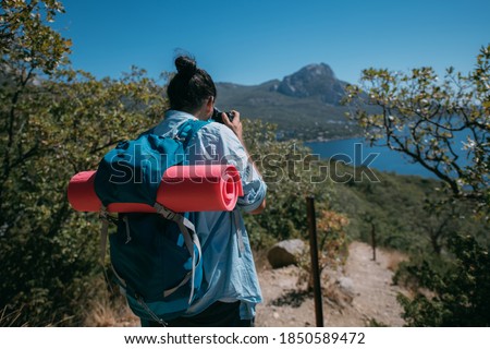 A man - a tourist with a backpack and a camera filming a landscape in the mountains. Young guy with camping equipment and a camera takes a photo or video near high rocks and blue sky