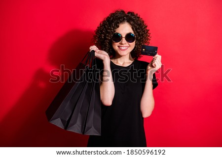 Photo of adorable pretty curly woman wear casual black outfit eyeglasses holding bags credit card isolated red color background
