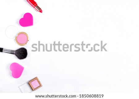 Cosmetics background. Make up brush, heart shaped sponge, red lipstick, pink eyeshadows and blusher on white. Copy space