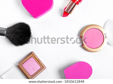 Cosmetics background. Make up brush, heart shaped sponge, red lipstick, pink eyeshadows and blusher on white. Copy space in the middle