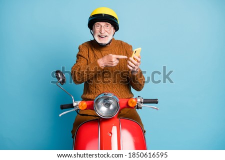 Portrait of his he nice attractive cheerful cheery glad bearded grey-haired man riding moped using demonstrating device notification isolated over blue pastel color background