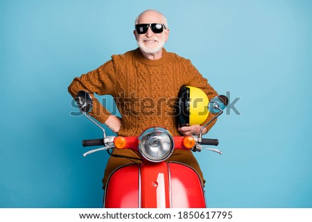 Portrait of his he nice attractive funky cheerful cheery content cool bearded grey-haired man hipster sitting moped rental service isolated over blue pastel color background