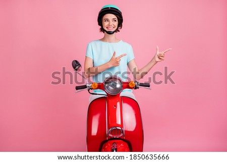 Photo of cheerful nice positive young lady ride red moped point empty space wear blue outfit slam isolated on pastel pink background