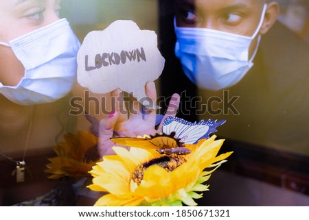 COVID-19 Lockdowns. Depressed and lonely couple looking through the window a butterfly during quarantine. People feeling sad as coronavirus pandemic forces couple to stay home in self isolation.