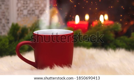 Red cup on the background of the New Year's interior, fireplace, candles, Christmas tree garland. Cozy winter evening by the fireplace. New Year and Christmas festive background.